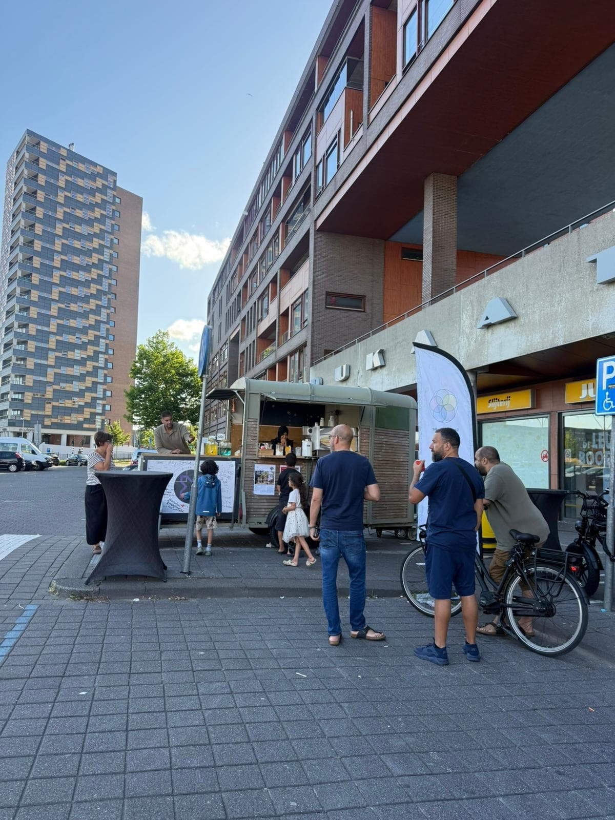 Buurtbewoners en kinderen rond de Koffiekar op een stoep tussen de flats van Osdorp