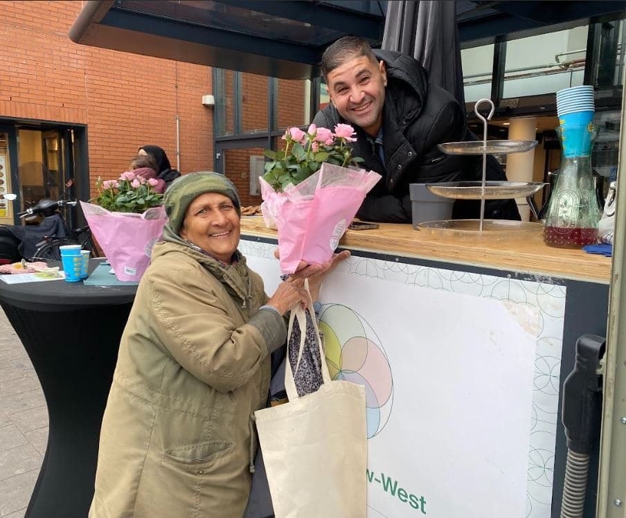 Bij de Koffiekar krijgt een lachende oudere buurtbewoonster een roze bloemetje van de barista