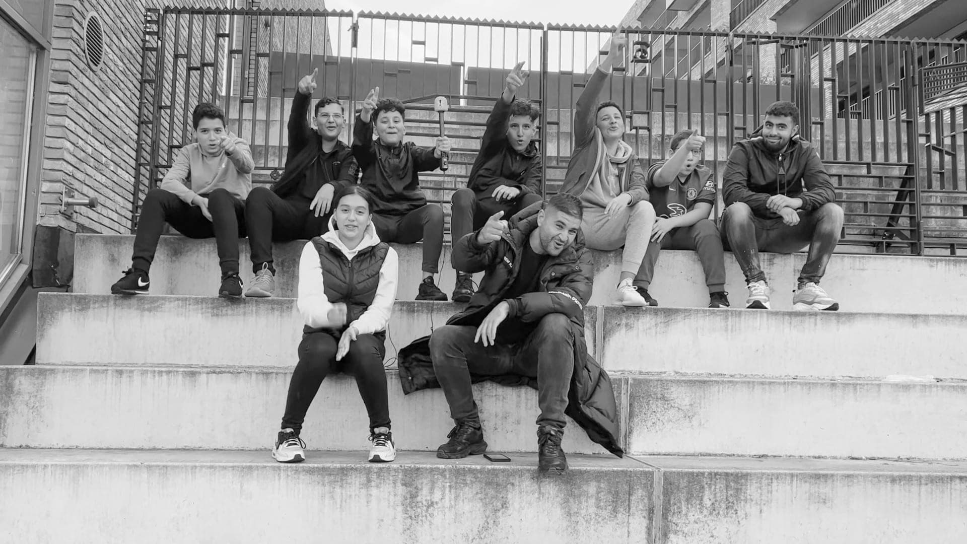 Zwart-witfoto van een groep jongeren van Young Osdorp United die op een betonnen trap zit en naar de camera wijst
